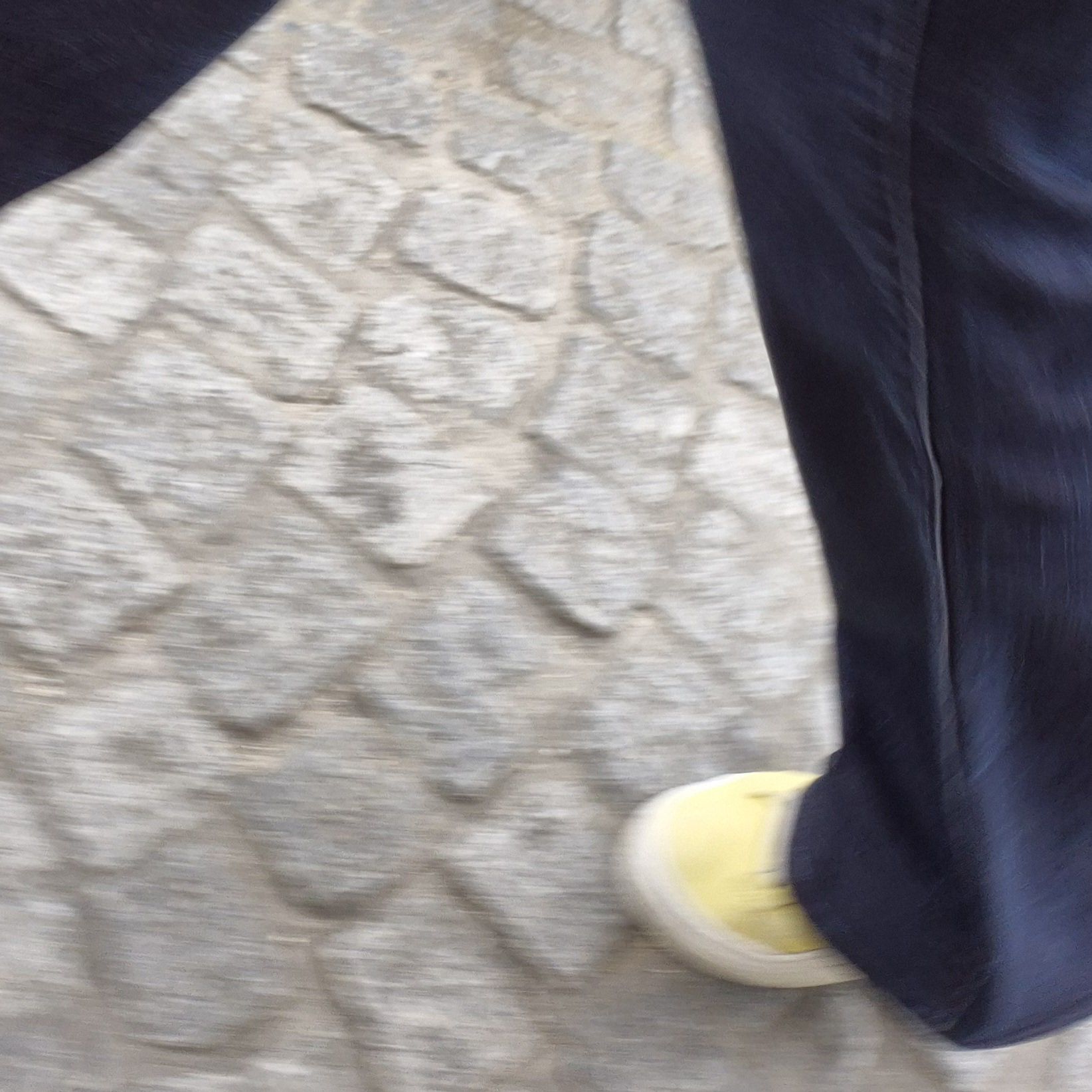 Kopfsteinpflaster mit einem gelben Schuh und in Jeans gekleideten Beinen.