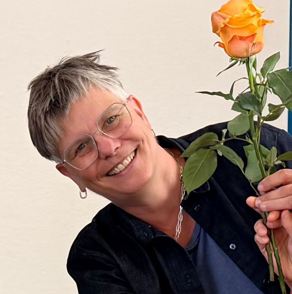 Portrait einer Frau mit Brille und oranger Rose in der Hand.