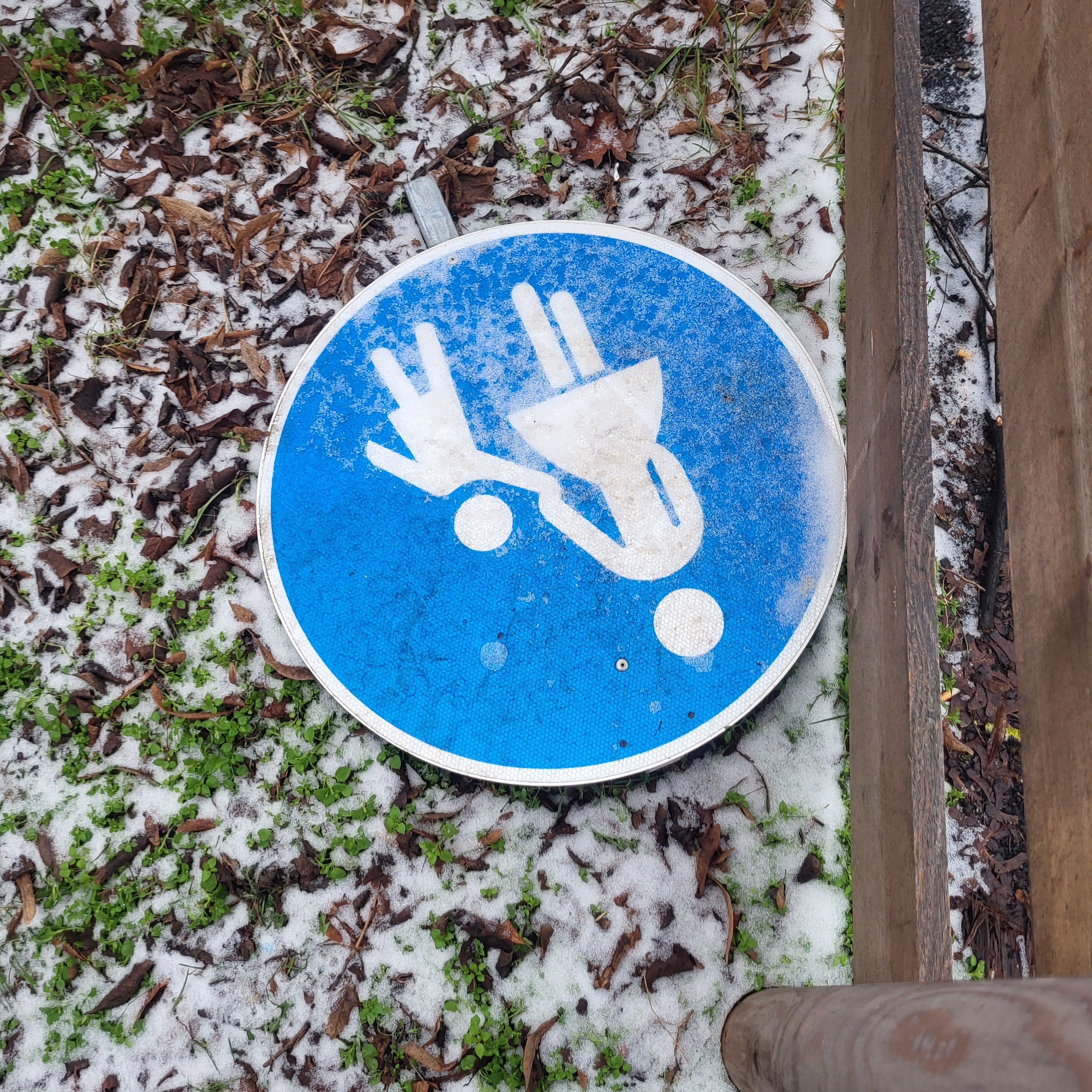 Ein blaues Verkehrsschild mit Mutter und Kind im Schnee am Boden liegend.