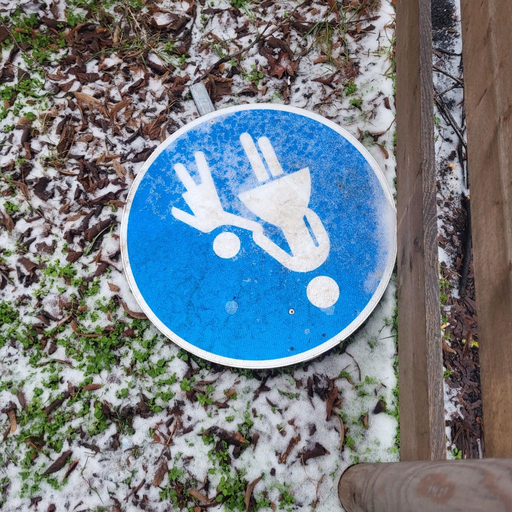 Ein blaues Verkehrsschild mit Mutter und Kind im Schnee am Boden liegend.