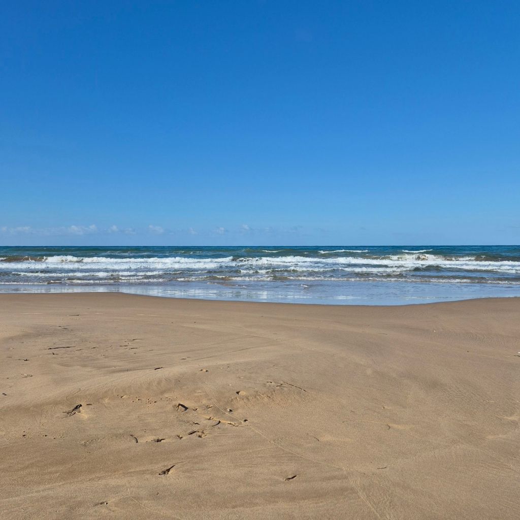 Weiter Sandstrand mit Brandung und blauem Himmel.