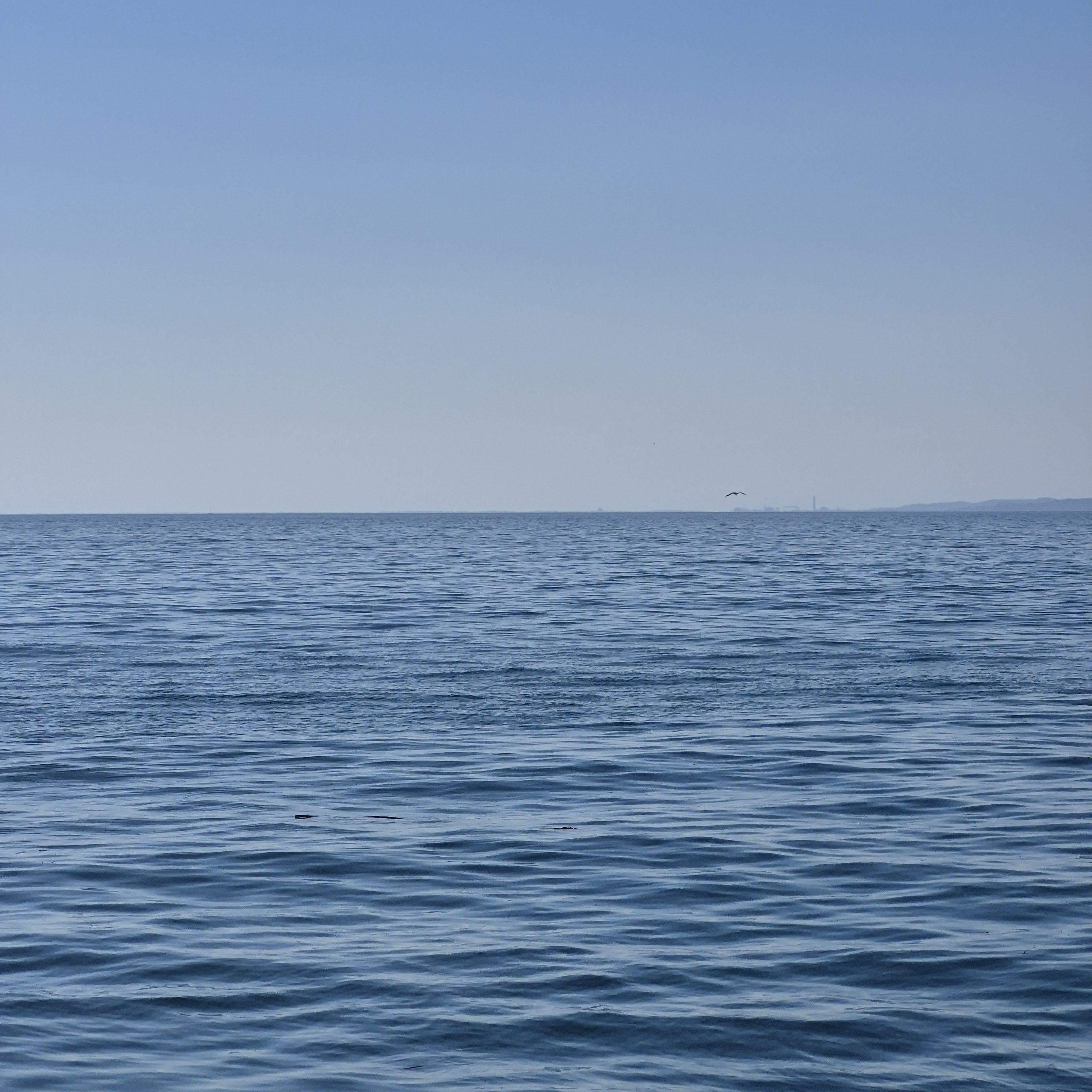 Blaues Meer mit gekräuselter Wasseroberfläche erstreckt sich bis zum hellblauen Horizont.