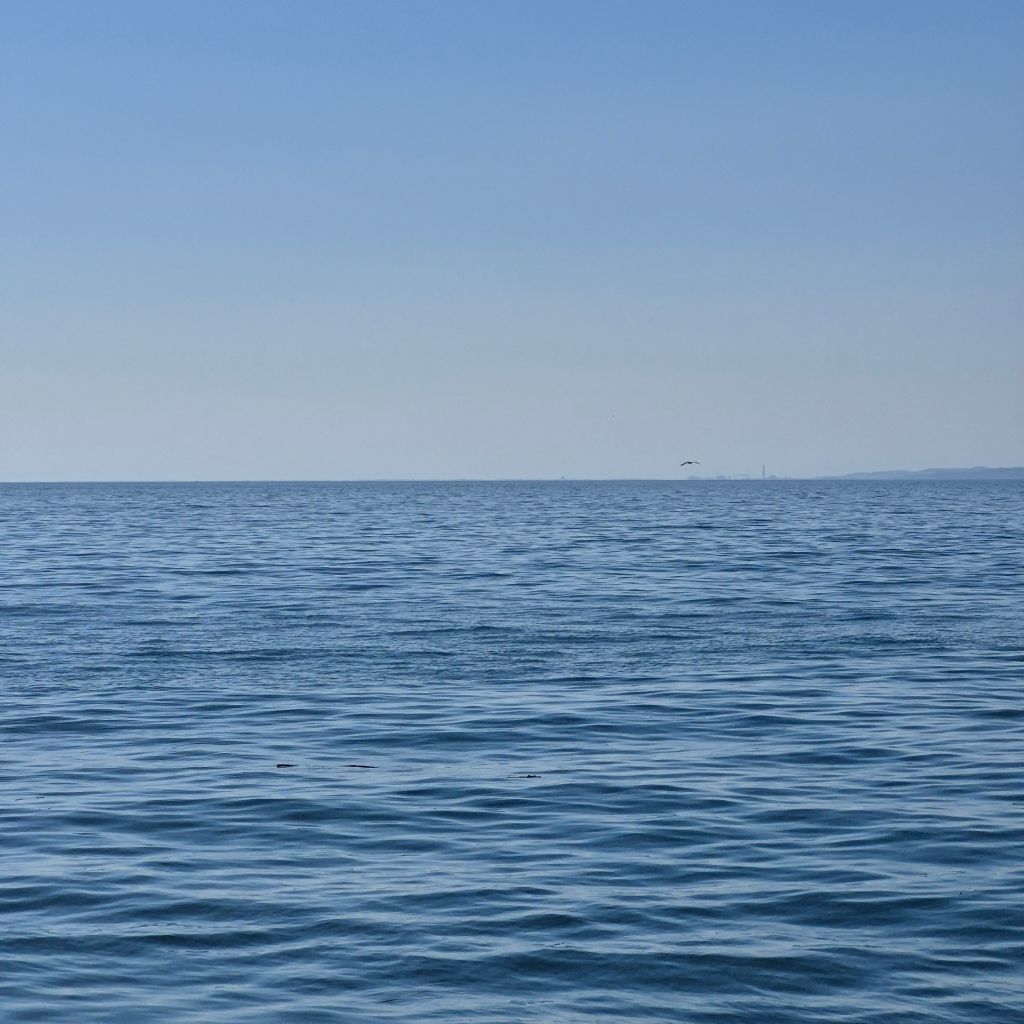 Blaues Meer mit gekräuselterWasseroberfläche erstreckt sich bis zum hellblauen Horizont.