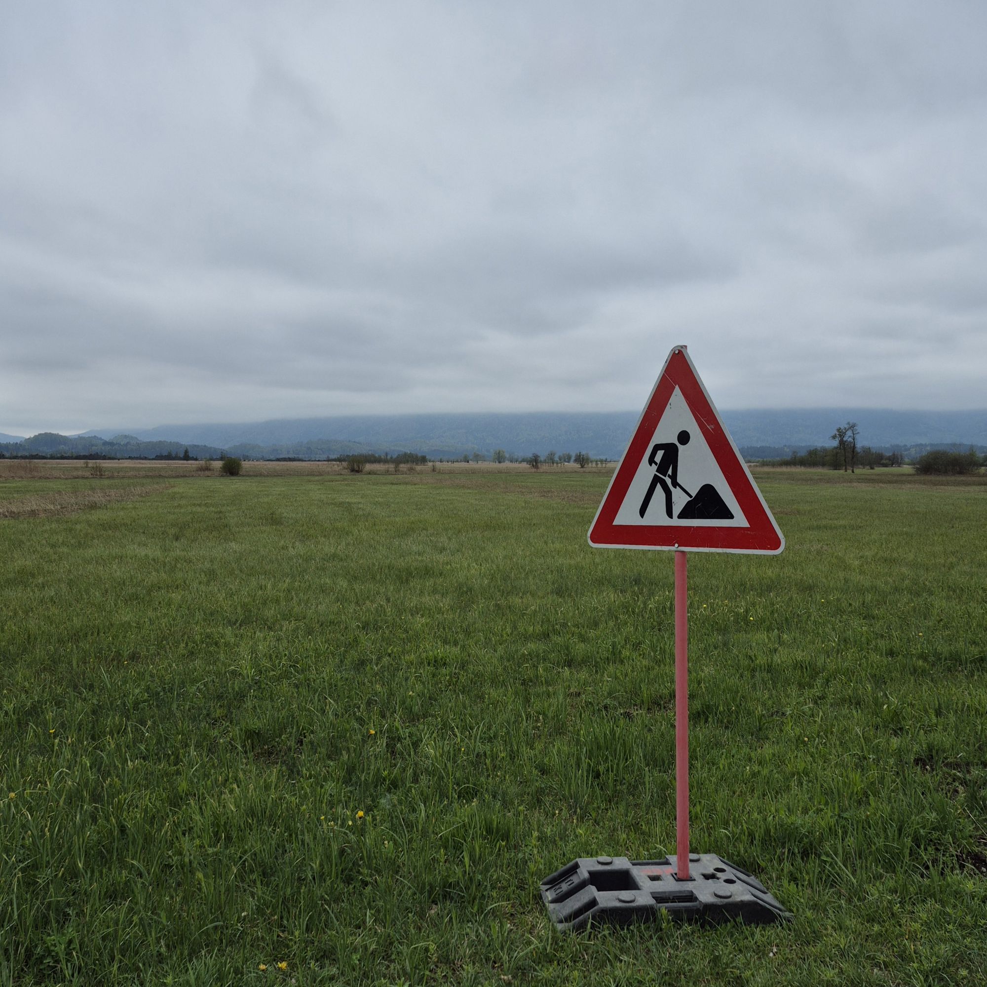 Baustellenschild auf einer weiten Wiese unter grauem Himmel – Symbol für Aufbruch, Übergang und Schall und Rauch.