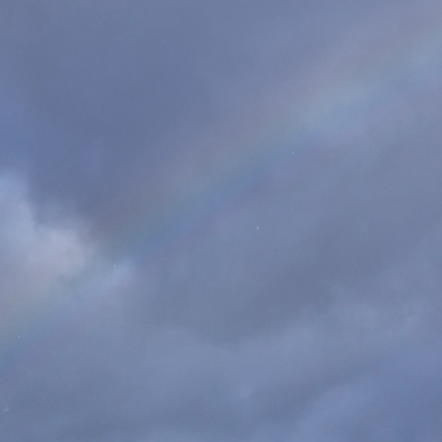 Schwach erkennbarer Regenbogen vor einem dunkel blaugrauem Wolkengebirge.