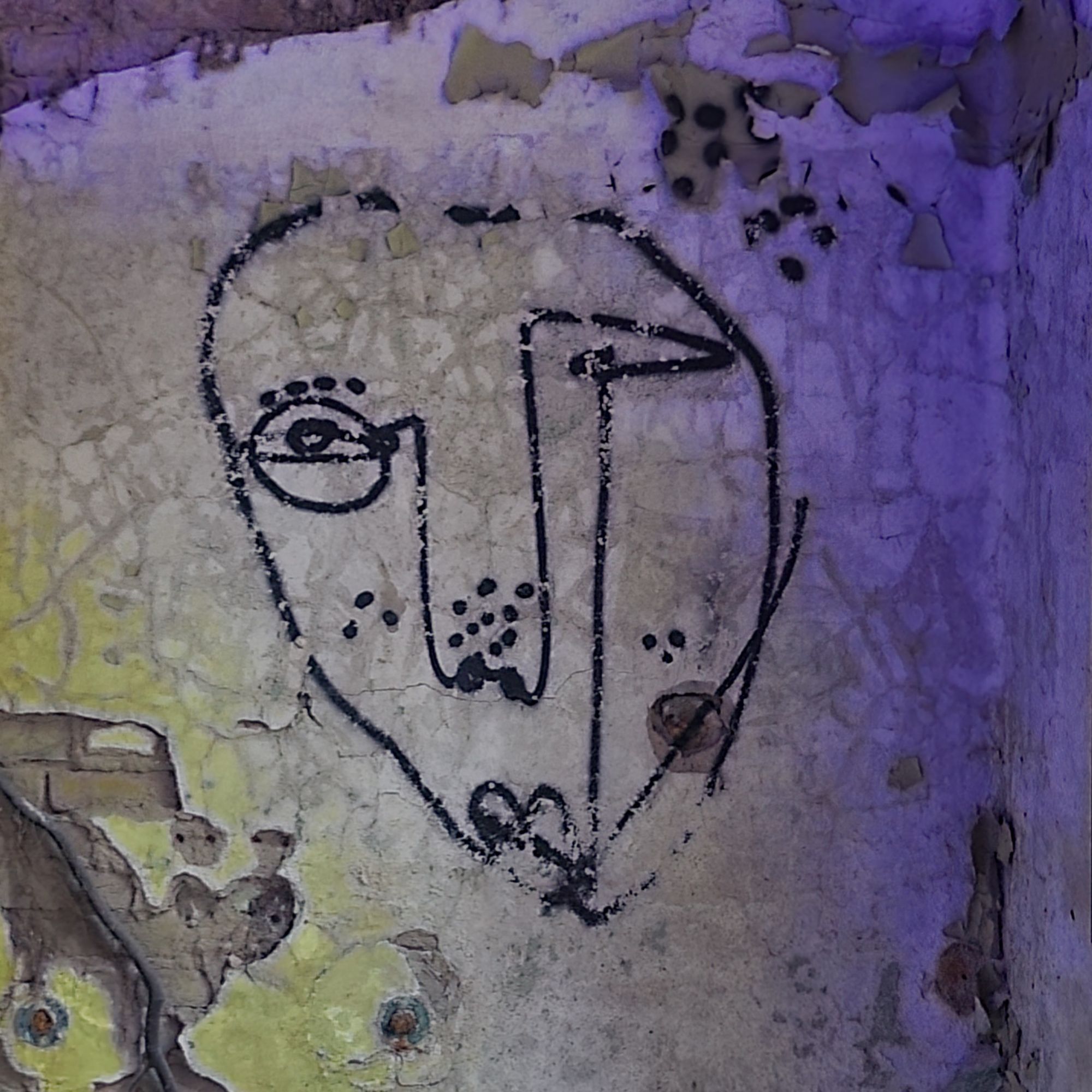 Entdecktes Graffiti eines abstrakt gezeichneten Gesichts auf einer verwitterten, abblätternden Wand, teilweise in violettes Licht getaucht.
